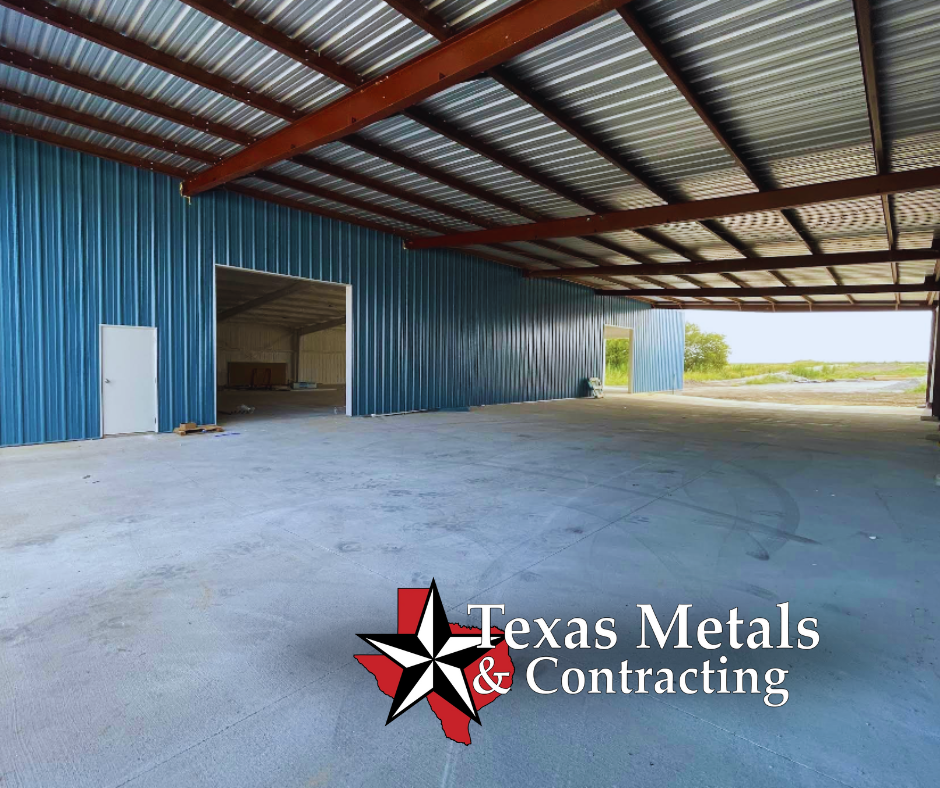 Lake Fork News Interior view of a spacious metal structure in East Texas, showcasing blue corrugated steel walls and a robust steel roof under natural daylight. Oversized doorways open to the rural landscape, capturing the distinctive “barndo”—barn-dominium—style popular in the region. The photograph emphasizes industrial craftsmanship and local architecture, with the Texas Metals & Contracting logo featured prominently at the lower right corner for clear attribution. Lake Fork, TX