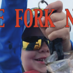 Lake Fork News A young child beams with pride as they hold up a freshly caught fish at Lake Fork, Texas. Wearing dark sunglasses and a bright blue jacket, the child's wide smile captures the excitement of the moment. Superimposed across the cheerful scene, bold red and blue headline text announces: "LAKE FORK NEWS JULY 2025 Online Edition Volume 1~6," marking this joyful catch as a feature in the local July edition. Lake Fork, TX